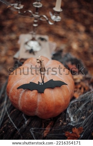 Big pumpkin at old tree stump with spider web and halloween horrible decor. Stack of old worn shabby books in leather binding silver candlestick with three burning white candles at fall leaves forest