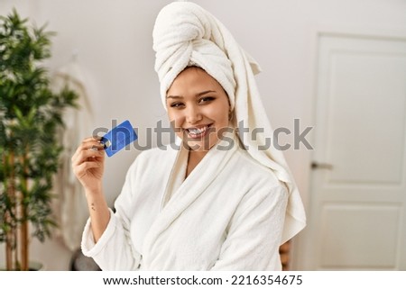 Young beautiful hispanic woman wearing bathrobe holding credit card at beauty salon