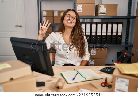 Young hispanic woman working at small business ecommerce showing and pointing up with fingers number four while smiling confident and happy. 