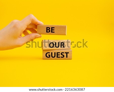Be our guest symbol. Concept word Be our guest on wooden blocks. Beautiful yellow background. Businessman hand. Business and Be our guest concept. Copy space