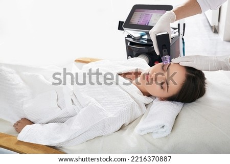 Pretty woman enjoying radiofrequency lifting procedure for her face skin rejuvenation at cosmetology. RF lifting Royalty-Free Stock Photo #2216370887