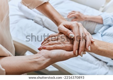 Relative holding trembling hand of senior woman with Parkinson's disease lying in hospital bed at medical ward. Diagnosis and treatment of Parkinson's disease and dementia Royalty-Free Stock Photo #2216370893