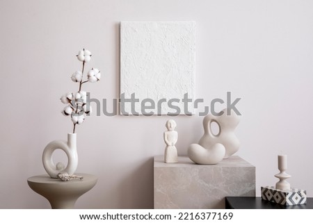 Creative composition of cozy and stylish living room with mock up paintings, marble cube, side table, ladder, decoration and personal accessories. Minimalist black and white home decor. Template.