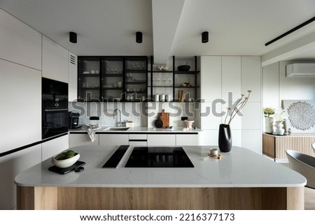 Modern composition of kitchen space with design kitchen island, grey table, black vase with flowers, furnitures and elegant personal accessories. Stylish home decor. Template. 
