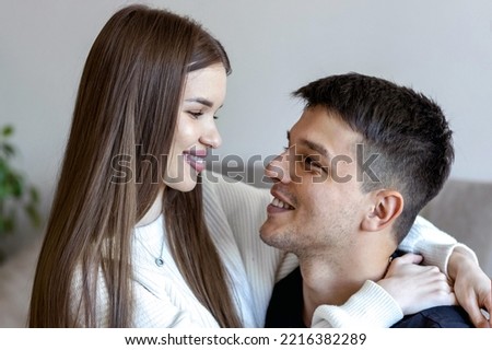 Portrait of a beautiful girl and a handsome guy. The girl sits in his arms, they look at each other with love and tenderness. Girl in casual winter denim clothes. Happy young people.