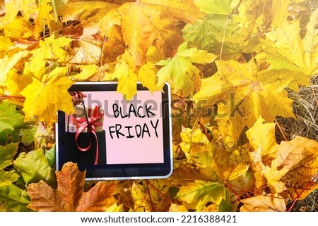 Black Friday sale concept. Tablet pad with sign Black Friday on screen, shopping bag, gift box over black background