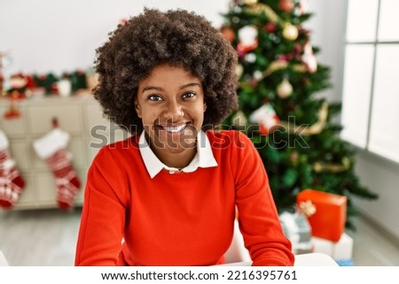 Young african american woman smiling confident sitting by christmas tree at home