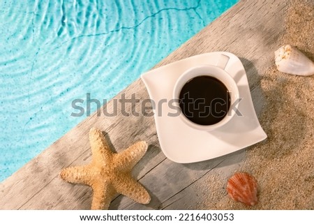 Coffee cup seen from above on a wooden pavement above a pool with a starfish. Ambiance vacation in summer.	