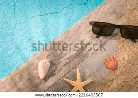 Sunglasses seen from above on a wooden pavement above a pool with a starfish. Ambiance vacation in summer.
