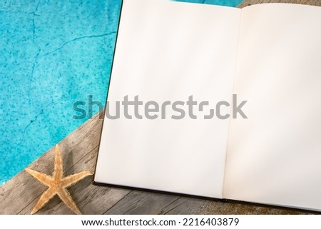 Open book without inscription seen from above on a wooden pavement above a pool with a starfish. Atmosphere vacations in summer.	
