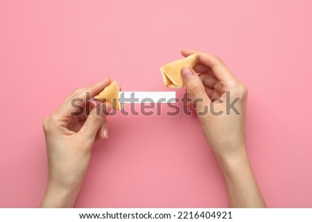 Woman holding tasty fortune cookie and paper with prediction on pink background, top view. Space for text Royalty-Free Stock Photo #2216404921