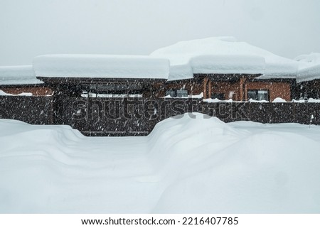 A private brick house and street covered with snow. There is a thick layer of snow on the roof of the house. It is snowing heavily. The snowy winter in Europe. The global problems of climate change Royalty-Free Stock Photo #2216407785