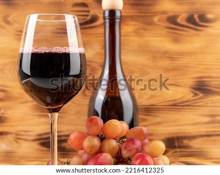 A glass of wine, a bottle of wine and grapes on a wooden background. Glass goblet with wine.