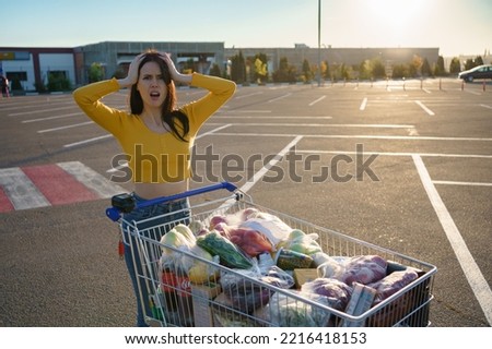 Young woman with shopping cart full of fresh and healthy food on the parking place near the supermarket