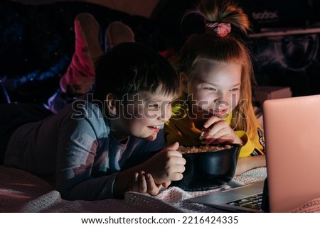 Overjoyed Kids sister brother laughing spend weekend free time together at home on couch bed eating popcorn. teen children watching video cartoon use remote control on laptop have fun. Movie night