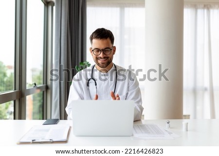 Portrait of man doctor talking to online patient on laptop screen sitting at clinic office desk giving online consultation for domestic health treatment. Telemedicine remote medical appointment