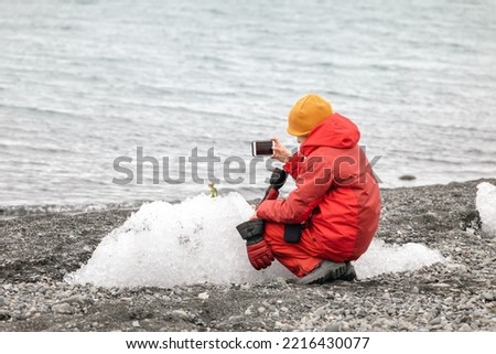 Girl taking pictures with her smartphone of her dinosaur on the ice near the glacier