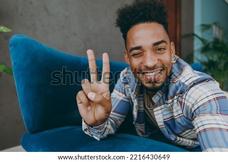Close up young man wear casual shirt lay down on blue sofa do selfie shot pov on mobile cell phone show v-sign stay at home rest relax spend free spare time in living room indoor People lounge concept