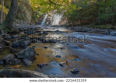 Golden light on the soft long exposure river and rocks with a beautiful forty-foot tall, fifty-foot-wide waterfall in background.