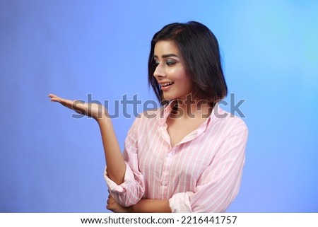 Portrait of a successful cheerful young girl presenting something with her hand with a happy smiling face and looking at the empty copy space camera.