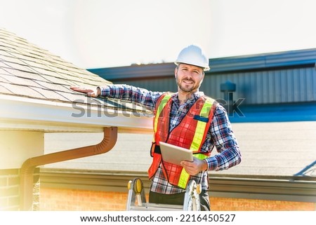 A man with hard hat standing on steps inspecting house roof Royalty-Free Stock Photo #2216450527