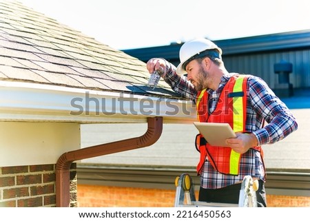 A man with hard hat standing on steps inspecting house roof Royalty-Free Stock Photo #2216450563