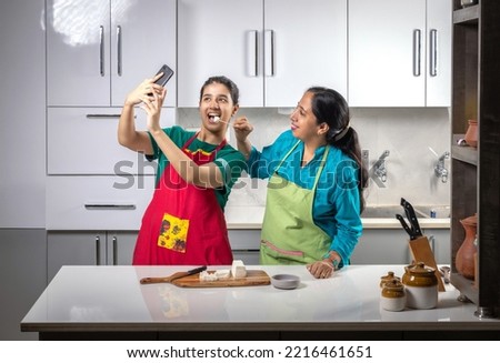 young girl taking pictures with her phone of herself with her mother while working in a kitchen