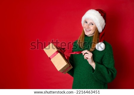 Merry Christmas Portrait of a beautiful young teenage girl in a cozy knitted green sweater and Santa's hat holding gift boxes. The red background is the place for the text. High quality photo