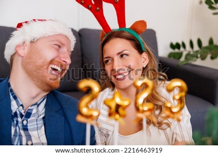 Cheerful young business people having fun celebrating Christmas at the office, holding little balloons shaped as numbers 2023 representing the upcoming New Year