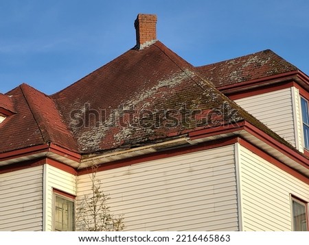 A red shingled rooftop that has mold and mildew covering most of the weathered shingles with lots of missing pieces on the shingles. Royalty-Free Stock Photo #2216465863