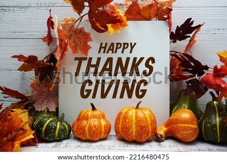 Happy Thanksgiving text message with autumn maple leaves and pumpkins on wooden background