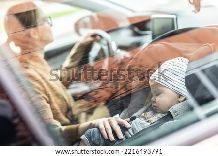 Mother concentrating on driving family car running errands while her baby sleeps in infant car seat by her site.