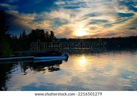 A picture of a pontoon boat on lake with a evening sunset