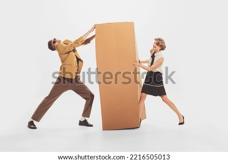 Portrait of young man and woman carrying giant cardboard boxes. New apartment furniture shopping. Moving into new flat. Concept of retro fashion, style, youth culture, emotions, ad