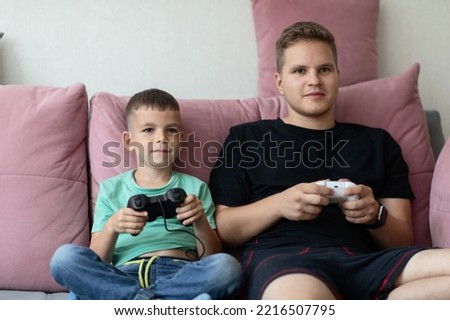 Two brothers with joysticks in their hands are playing computer games comfortably sitting on the couch at home. online games with friends, selective focus