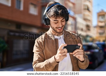 Young hispanic man smiling confident playing video game at street