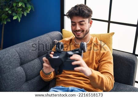 Young hispanic man smiling confident holding virtual reality glasses at home