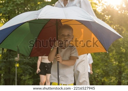Grandson and grandfather to move out in the park under a bright umbrella at sunset. A pensioner and a little boy spend their free time on weekends together..
