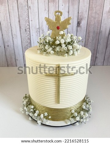 Cake for religious celebrations like wedding, christening, with a golden cross on the front and an angel on top of the cake. on a white plate, isolated. Front view.
