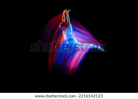 Levitation. One flying, jumping dancer or gymnast performing tricks in the air over black background with mixed neon glowing rays. Fantasy, cyberpunk, sport, fashion