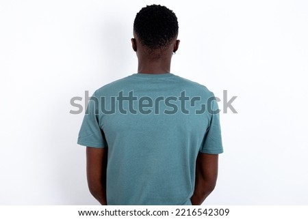 young handsome man wearing green T-shirt over white background standing backwards looking away with arms on body.