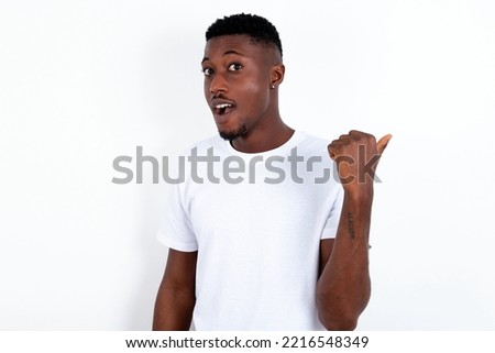 Impressed young handsome man wearing white T-shirt over white background point back empty space