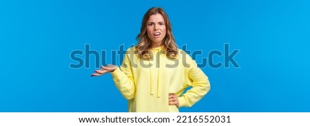Whats wrong, why. Confused and frustrated blond girl dealing with person complains, shrugging and raise one hand in dismay grimacing perplexed, look camera questioned, blue background. Royalty-Free Stock Photo #2216552031