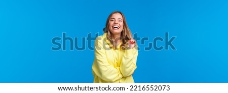 Happy blond young girl laughing from funny joke, having conversation with friends standing near university campus enjoying being in hilarious company, standing blue background.