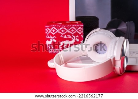 Festive red composition with white laptop computer, headphones, big cup for hot chocolate. Christmas mood and vibe, listen traditional new year songs music. Preparation for Christmas background
