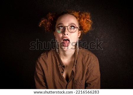 Crazy woman portrait on black dark background. The red haired girl makes a face, sticks out her tongue and rolls her eyes.