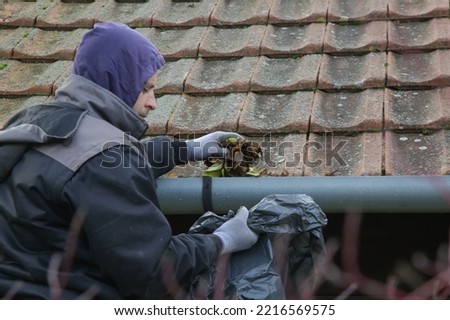 Man cleaning the gutter from autumn leaves before winter season. Roof gutter cleaning process.	 Royalty-Free Stock Photo #2216569575