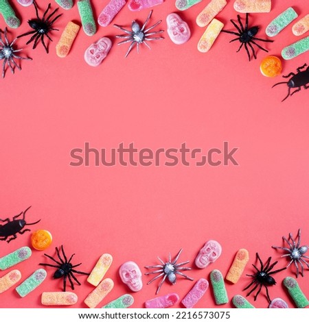 Halloween sweet background frame with scary pumpkin cookies, candy and Halloween decor on pink table, copy space, top view