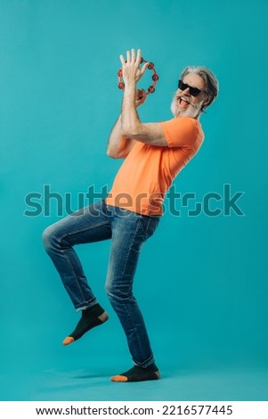 Elderly gray-haired bearded man dances with a tambourine. Studio photo on a colored background.