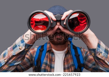Discovering new places. Confident young bearded man carrying backpack and looking through binoculars while standing against grey background Royalty-Free Stock Photo #221657923